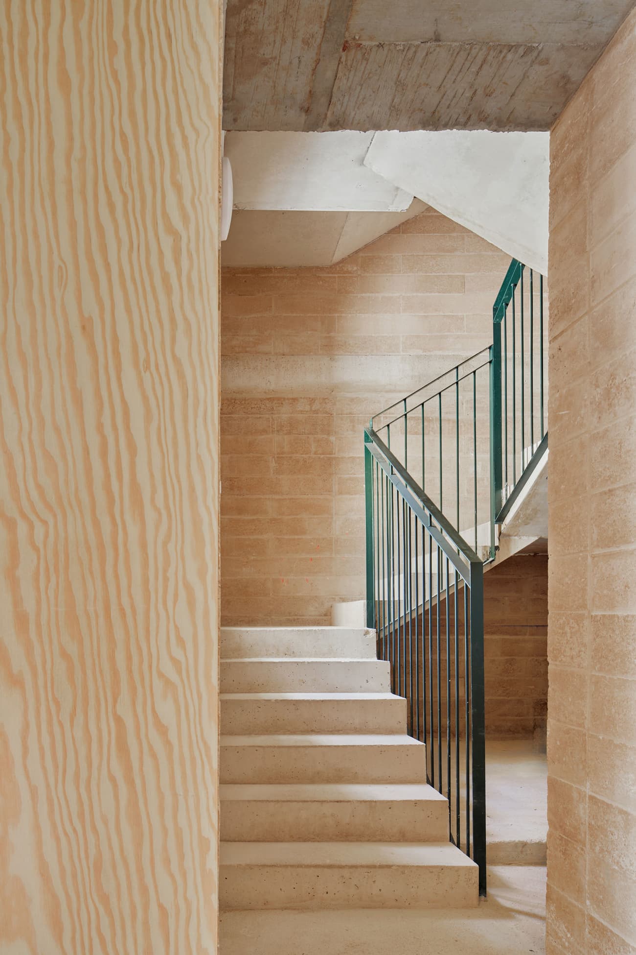 Architectural project - metal railing, concrete finish, exposed concrete, thoughtful design, concrete stairs, minimalist stairs, raw concrete, modern staircase, sleek railing, wood wall, concrete structure, vertical lines, efficient use, interior stair, smart design, textured surfaces, warm interior, architectural detail, sustainable materials, industrial design, warm tones, natural tones, eco design, neutral tones, industrial vibe, beige, light wood, natural wood, industrial style, functional design, compact space, simple design, Scandinavian style, light brown, minimalist design, plywood wall, clean lines, timber cladding, wood cladding, cozy vibe, textured wall, structural element, inviting space, black railing, nordic influence, timber wall, modern interior, minimalist interior, staircase, efficient design, residential interior, stairwell