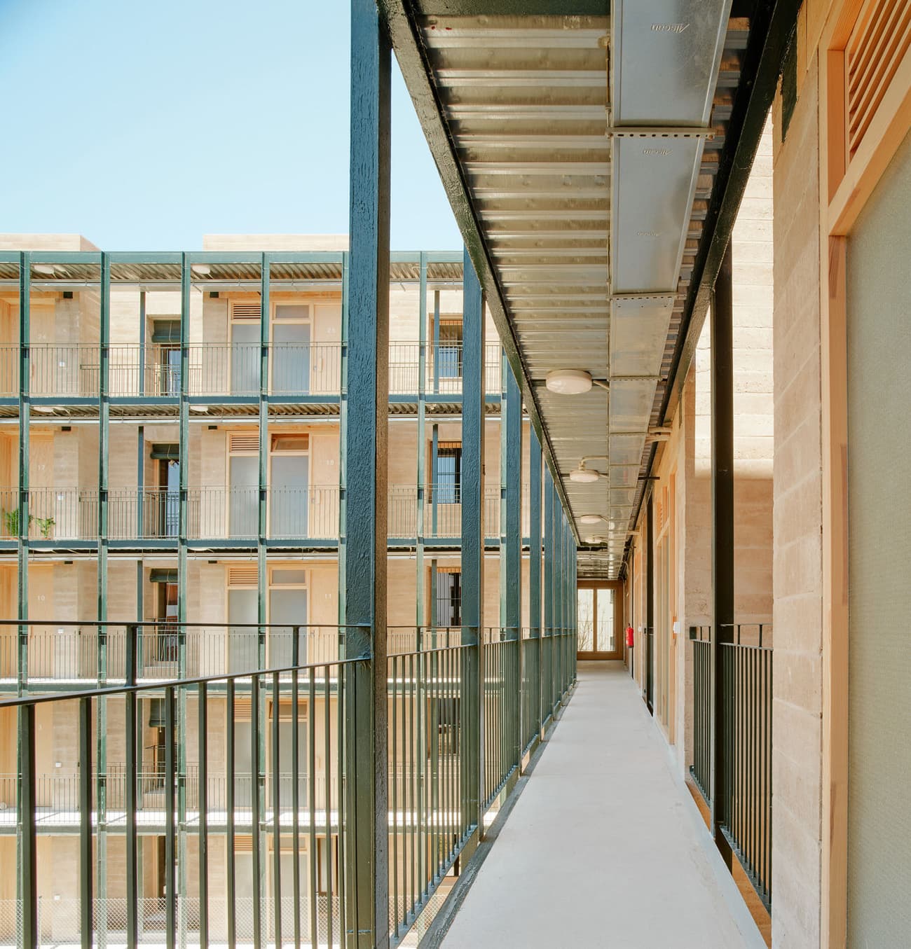 Architectural project - metal railing, linear design, residential complex, exterior walkway, outdoor corridor, open walkway, repetitive elements, geometric lines, iron railing, exterior material, outdoor circulation, rhythmical facade, corner detail, repetitive facade, facade expression, urban fabric, interconnected spaces, modular architecture, outdoor access, circulation design, exterior interaction, facade articulation, iron, warm stones, light play, steel, metal, modular design, industrial aesthetic, neutral tones, daylight, beige, concrete, structural design, minimalist facade, light wood, airy design, sunlight, contemporary design, industrial touch, steel structure, urban design, modular structure, modern architecture, exterior elements, residential architecture, open air, minimalist exterior, sky view, facade design, light facade, facade rhythm, architectural rhythm, sustainable living, apartment building, exterior pattern, efficient design, city dwelling, urban living, modern materials
