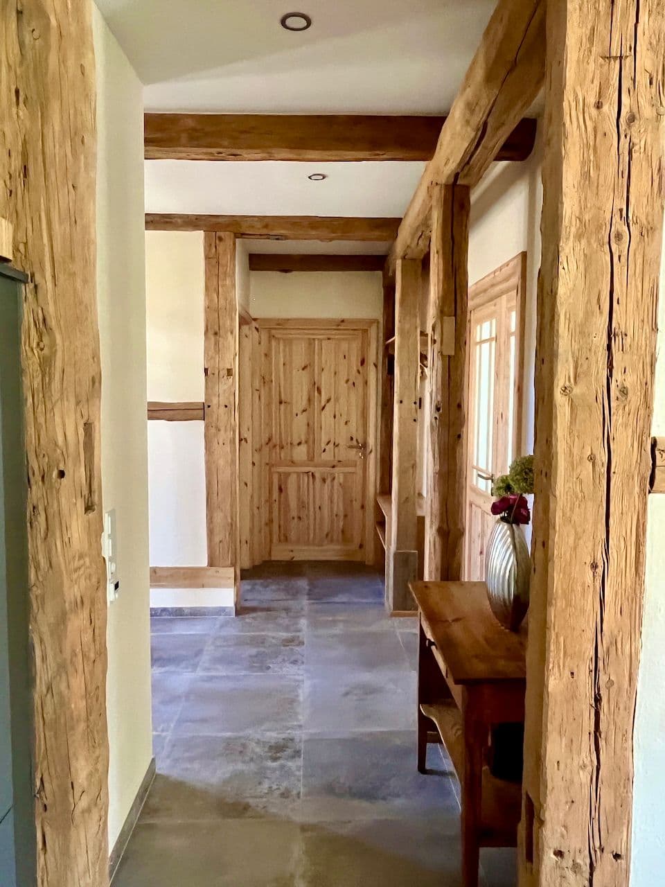 Architectural project - vintage touch, country house, rustic hallway, wood columns, classic style, warm interior, natural materials, soft lighting, eco-friendly design, sustainable materials, wood, timber, natural light, warm tones, grey, neutral tones, exposed beams, beige, brown, natural wood, wooden beams, farmhouse style, timber beams, natural textures, rustic charm, timber walls, cozy vibe, stone, wooden table, inviting space, earthy tones, stone tiles, traditional design, warm light, country vibe, stone floor, wooden cladding, timeless design, cozy home, home corridor, rustic decor, wooden door, wooden walls, residential hallway
