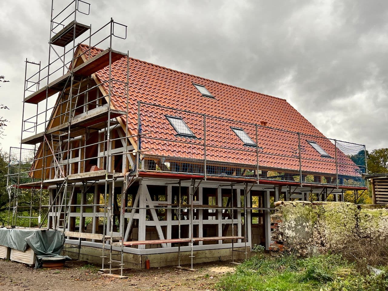 Architectural project - skylights, rustic materials, red tiles, terracotta roof, farmhouse, rooftop, framework, wood, timber, scaffolding, outdoor space, timber frame, natural light, eco design, grey, neutral tones, timber structure, under construction, construction process, building site, brown, open structure, wooden beams, rural architecture, natural textures, open framework, exterior, low carbon, circular design, sustainable home, passive house, landscape integration, Nordic style, countryside home, energy efficient, stone, rustic style, sloped roof, pitched roof, terracotta, stone wall, rural setting, traditional style, earthy palette, renovation, rural house, clay tiles, red, remodel