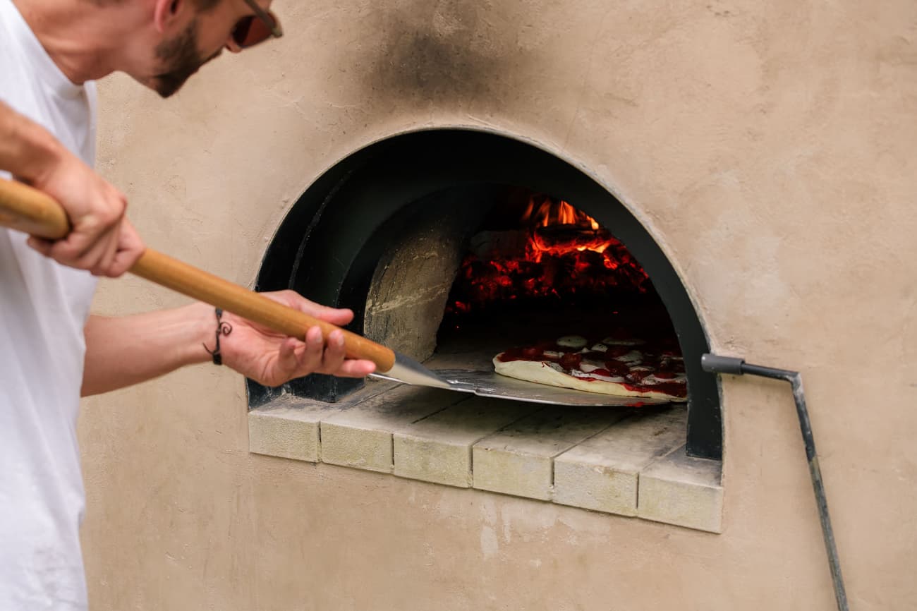 Architectural project - natural materials, warm tones, beige, cozy vibe, plaster wall, stone, plaster, rustic style, outdoor oven, pizza oven, wood-fired oven, stone oven, outdoor cooking, alfresco dining, rustic cuisine, artisan baking, firewood cooking, handcrafted pizza, kitchen tools, outdoor kitchen, outdoor cooking space, terracotta wall, clay oven, traditional oven, pizza making, culinary art, oven fire, baking tools, earthy tones, warm atmosphere, food preparation, summer cooking, garden dining, dining experience, outdoor meal, entertaining space, family gathering, casual dining, homemade pizza, stone tiles, brick oven, backyard kitchen, clay