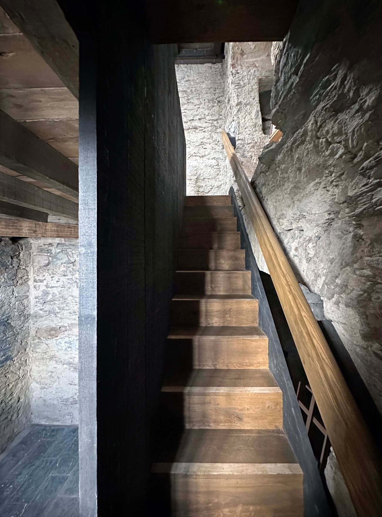 Architectural project - interior stair, exposed stone, heritage design, rustic interior, muted colors, historic building, vintage feel, atmospheric space, rustic stairs, timber stairs, moody atmosphere, intimate space, architectural detail, wood, timber, raw materials, grey tones, warm tones, natural tones, grey, beige, brown, rustic vibe, rustic modern, rustic charm, industrial touch, cozy space, natural finish, warm wood, plaster wall, stone, plaster, earthy tones, stone wall, cozy corner, textured walls, renovation, dark tones, stone texture, remodel
