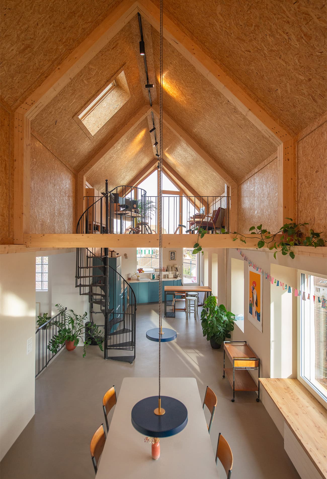 Architectural project - flexible living, metal stairs, blue accents, family dining, home dining, loft space, house plants, OSB board, pendant lighting, creative workspace, colorful art, warm interior, natural materials, eco-friendly design, wood, timber, metal, natural light, inviting atmosphere, warm tones, green, beige, concrete, light wood, multifunctional space, functional design, blue, Scandinavian vibe, timber walls, modern rustic, biophilic design, sustainable home, Nordic style, cozy kitchen, airy space, open layout, open plan, casual dining, modern living, cozy home, skylight, indoor plants, high ceiling, double height, wood interior, vaulted ceiling
