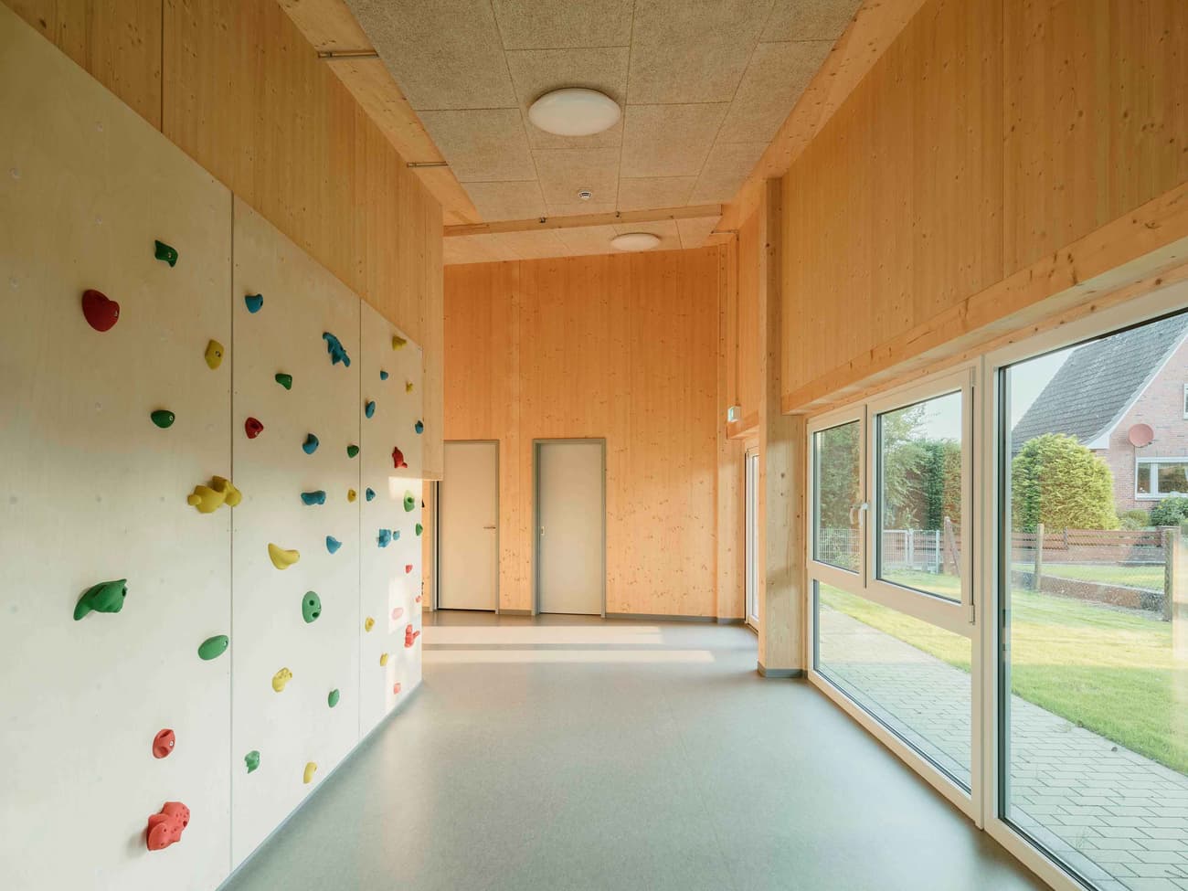 Architectural project - indoor play, spacious room, vibrant environment, minimal design, cozy interior, natural materials, eco-friendly design, sustainable materials, wood, timber, natural light, pastel colors, modular design, community space, grey, neutral tones, daylight, beige, light wood, honey wood, Scandinavian style, recreation area, glass doors, timber panels, wood panels, clean lines, Nordic design, timber interior, warm atmosphere, playful vibe, multifunctional room, bright interior, sliding doors, open space, educational space, playful space, learning environment, family-friendly, wood interior
