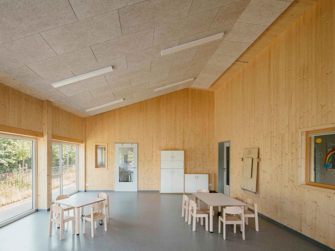Architectural project - flexible space, off-white, spacious room, welcoming environment, modular furniture, acoustic panels, simple interior, minimal design, cozy interior, warm interior, indoor space, eco-friendly design, sustainable materials, wood, timber, natural light, inviting atmosphere, green building, community space, neutral tones, daylight, beige, light wood, natural wood, honey wood, Scandinavian style, light tones, timber walls, window view, wood walls, open layout, child friendly, bright space, nordic influence, educational space, soft colors, informal seating