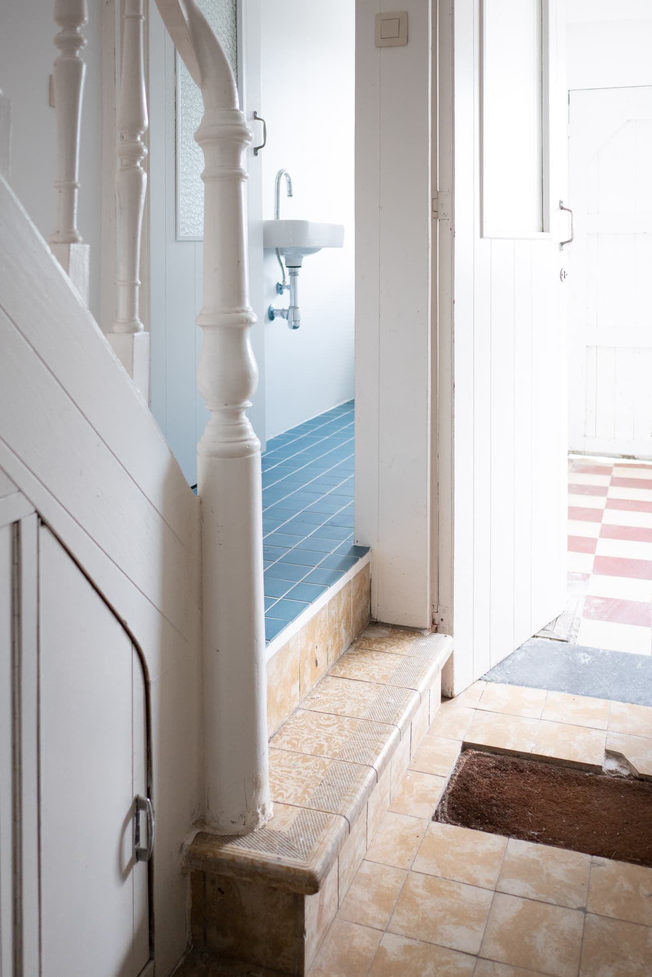 Architectural project - retro style, narrow hallway, vintage vibe, white door, entrance hall, old-world charm, entrance, checkerboard floor, blue tiles, light blue, natural light, natural tones, neutral tones, daylight, beige, compact space, cozy space, white walls, white, residential, interior space, wooden staircase, practical design, ceramic tiles, stairwell