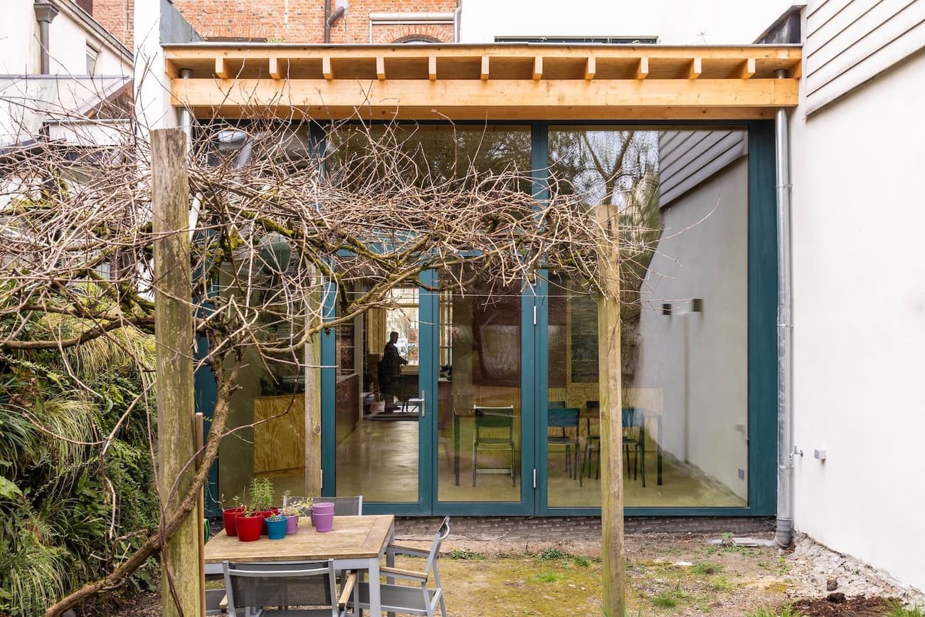 Architectural project - minimalist garden, green view, modern extension, patio, wooden pergola, backyard, residential extension, house extension, timber canopy, small patio, urban extension, outdoor table, outdoor chairs, maple wood, natural materials, timber, steel, outdoor space, natural light, glass, warm tones, contemporary style, green, daylight, beige, brown, light wood, multifunctional space, eco friendly, modern design, compact space, minimalist design, neutral colors, Scandinavian vibe, sustainable building, earth tones, stone, open plan, garden dining, cozy atmosphere, nature connection, bright interior, family home, sliding doors, urban garden, glass facade, indoor outdoor flow