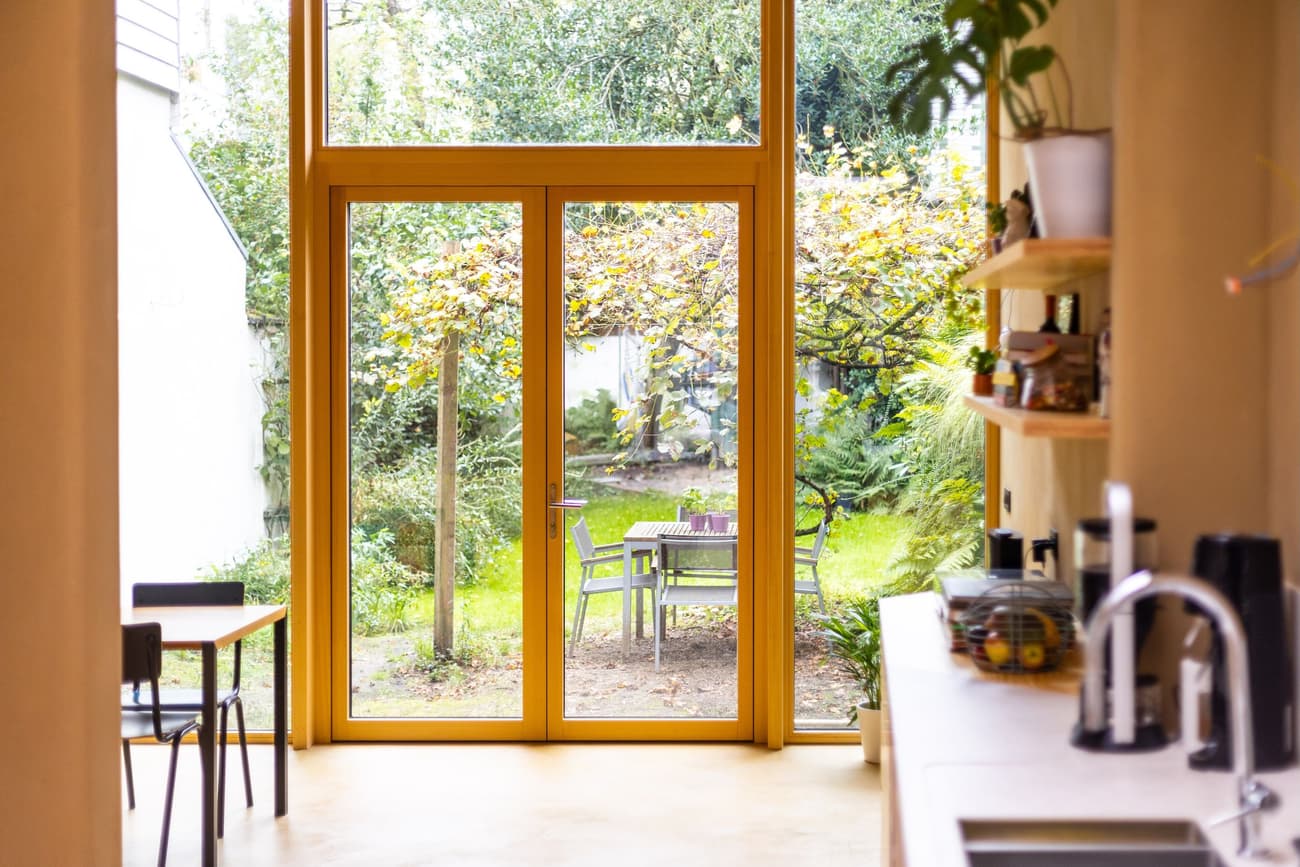 Architectural project - cozy dining, indoor garden, open doors, compact layout, kitchen view, dining nook, tall windows, simple shelves, cottage charm, lush view, warm interior, natural materials, wood, timber, timber frame, natural light, sustainable design, glass, natural tones, green, neutral tones, functional space, beige, eco friendly, modern design, Scandinavian style, relaxed atmosphere, yellow accents, earth tones, passive house, light filled, indoor outdoor, white, inviting home, wood frame, green living, family kitchen, nature connection, Nordic vibe, integrated design, minimalist kitchen, breakfast nook, bright space, practical space, seamless transition, open shelving, floor to ceiling, homey feel, garden access
