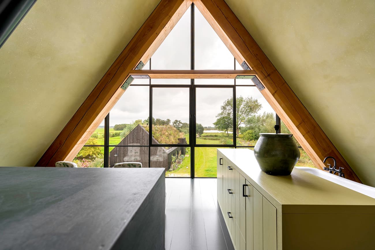 Architectural project - triangular window, attic conversion, pastoral setting, A-frame house, creative workspace, painted floor, wood, timber, steel, timber frame, natural light, sustainable design, glass, warm tones, eco design, exposed structure, green, neutral tones, daylight, beige, light wood, natural wood, simple design, honey wood, wood beams, rustic modern, minimalist design, black, modern rustic, scenic view, clean lines, large windows, indoor outdoor, timber cladding, wood cladding, cozy vibe, countryside view, airy space, timber interior, open layout, open plan, panoramic view, inviting space, peaceful retreat, cozy corner, tranquil atmosphere, warm vibe, green design, home office, minimalist aesthetic, bright interior, black countertop, glass facade, ceramic vase
