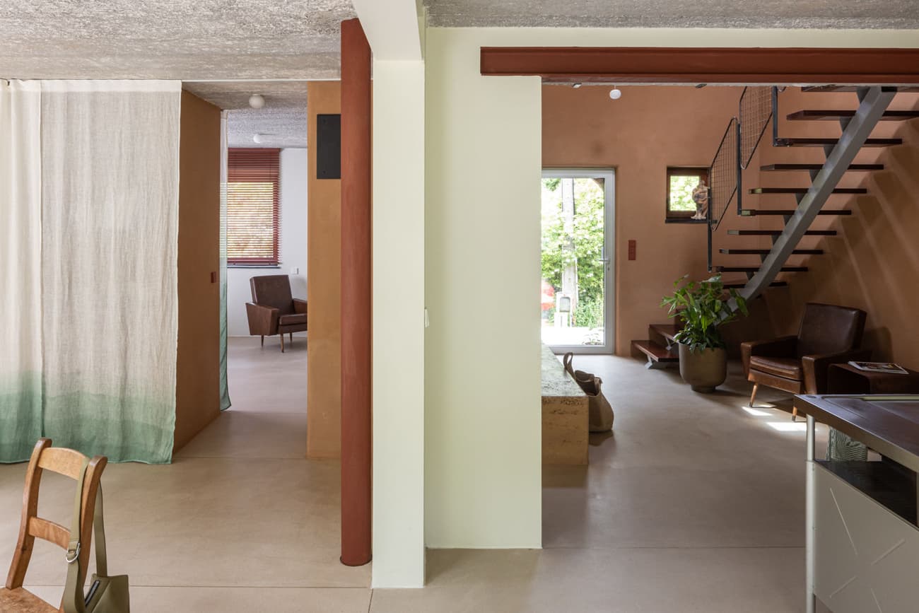 Architectural project - beige walls, brick wall, natural elements, room divider, living room, fabric curtain, exposed brick, indoor green, potted plant, open stair, cantilevered stair, Scandi style, welcoming atmosphere, wood furniture, leather chair, warm interior, wood, timber, city living, fabric, relaxed vibe, natural light, sustainable design, warm tones, neutral tones, daylight, beige, brown, concrete, Scandinavian influence, natural textures, minimalist design, soft textures, eco-friendly materials, timber elements, modern rustic, contemporary home, white, wood accents, casual living, open layout, open plan, terracotta wall, earthy tones, terracotta, brick, residential space, lounge area, simple decor, concrete floor, home interior, cozy home, smooth finish, urban apartment, staircase, red