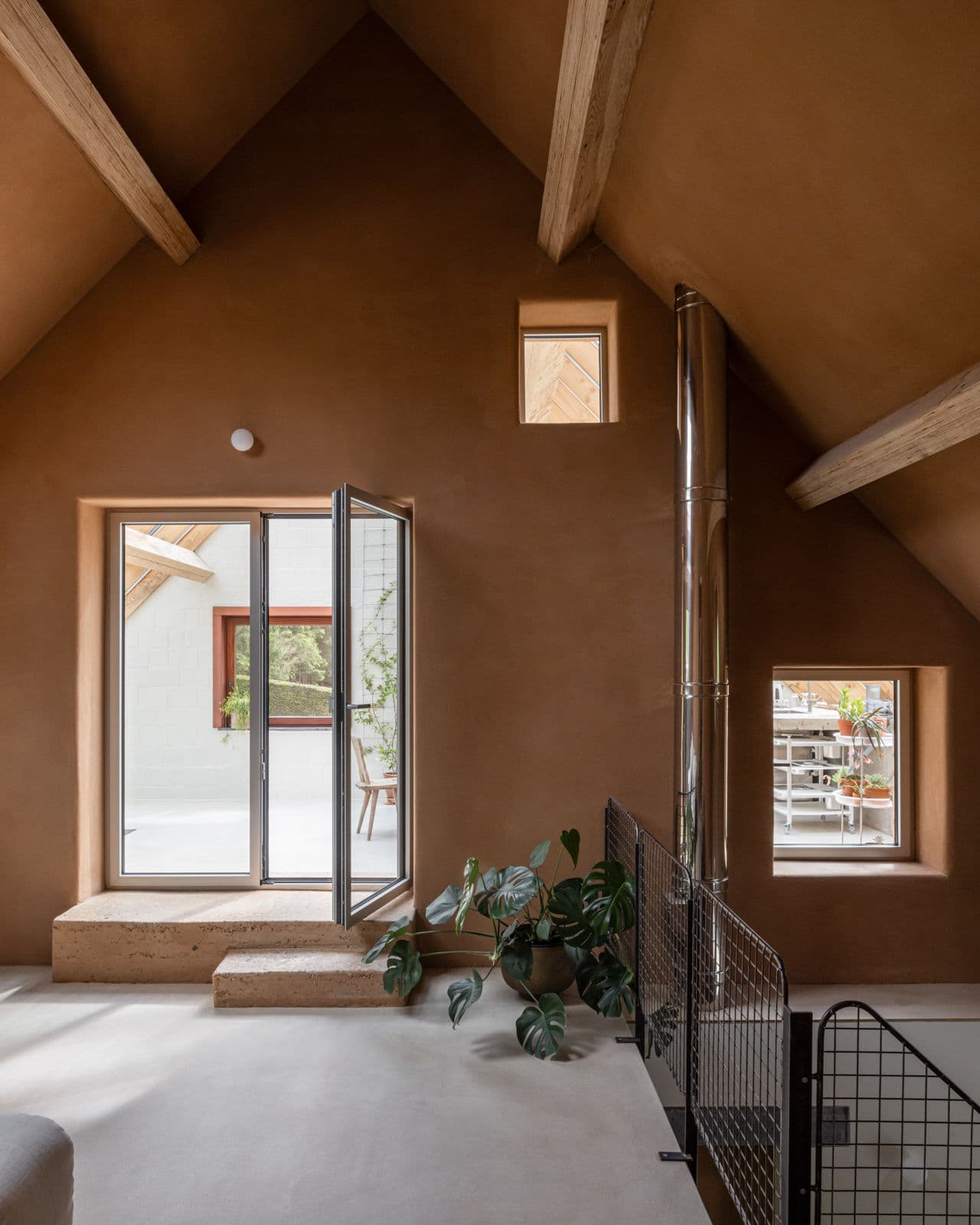 Architectural project - metal railing, textured surfaces, warm interiors, hygge, loft space, attic room, clay walls, houseplant, open door, patio view, peaceful home, natural materials, raw materials, natural light, sustainable design, multifunctional area, exposed beams, daylight, wooden beams, rustic modern, private retreat, industrial touch, minimalist style, neutral palette, relaxation spot, Scandinavian vibe, earth tones, modern rustic, passive house, eco friendly home, cozy vibe, Nordic style, energy efficient, small space, cozy nook, inviting space, minimalist decor, warm atmosphere, pitched roof, modern home, compact living, plaster walls, brown tones, indoor plant, skylight, home renovation, garden access, vaulted ceiling