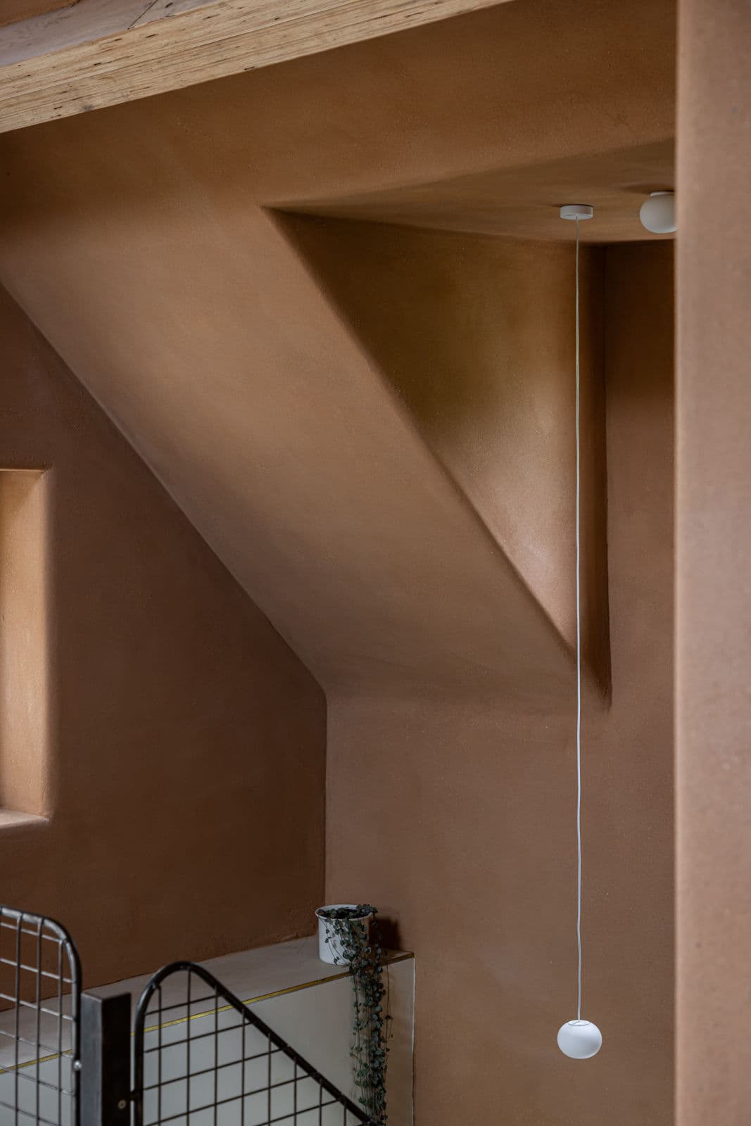 Architectural project - rustic interior, earth wall, geometric elements, sculptural design, white pendant, ceiling light, natural lighting, recessed window, architectural focus, wall niche, mindful living, materiality, earthen architecture, warm interior, natural materials, architectural detail, sustainable materials, shadow play, warm tones, eco design, sustainable architecture, neutral tones, daylight, intimate corner, rustic charm, contemporary design, minimalist design, natural finish, rammed earth, modern rustic, architectural simplicity, simple elegance, cozy vibe, textured wall, plaster wall, inviting space, earthy tones, minimalist aesthetic, pendant light, smooth surfaces, soft light, organic textures