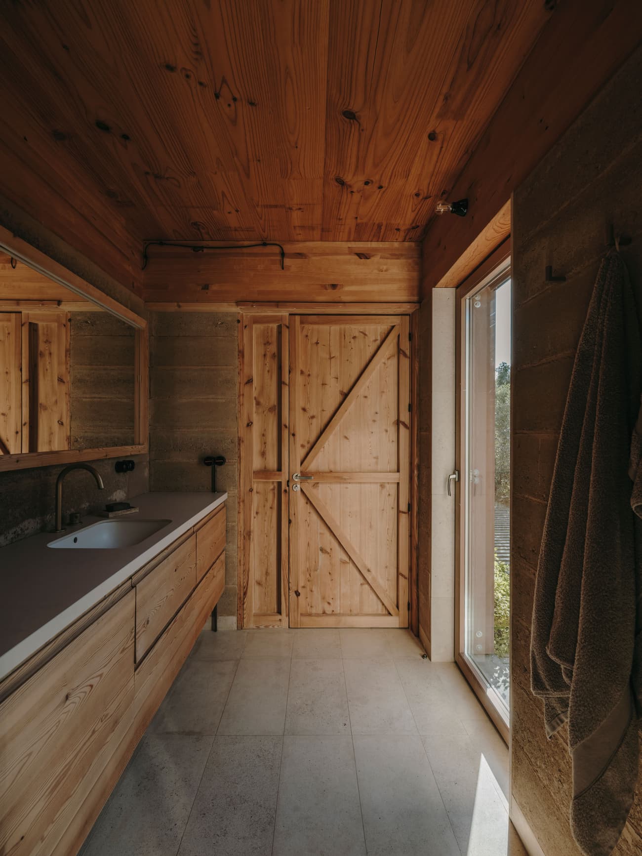 Architectural project - raw finishes, exposed pipes, countryside charm, rustic bathroom, farmhouse bathroom, sliding barn door, cozy bathroom, Nordic touch, polished floor, double sink, simple vanity, small bathroom, zen retreat, spa-like vibe, organic feel, warm interior, natural materials, eco-friendly design, sustainable materials, wood, timber, natural light, warm tones, neutral tones, daylight, beige, brown, concrete, compact space, natural textures, industrial touch, neutral palette, minimalist design, Scandinavian vibe, window view, stone, warm ambiance, rustic style, green home, earthy tones, stone floor, functional layout, wood ceiling, peaceful atmosphere, timber wall, wood paneling, concrete wall, built-in storage, timber door