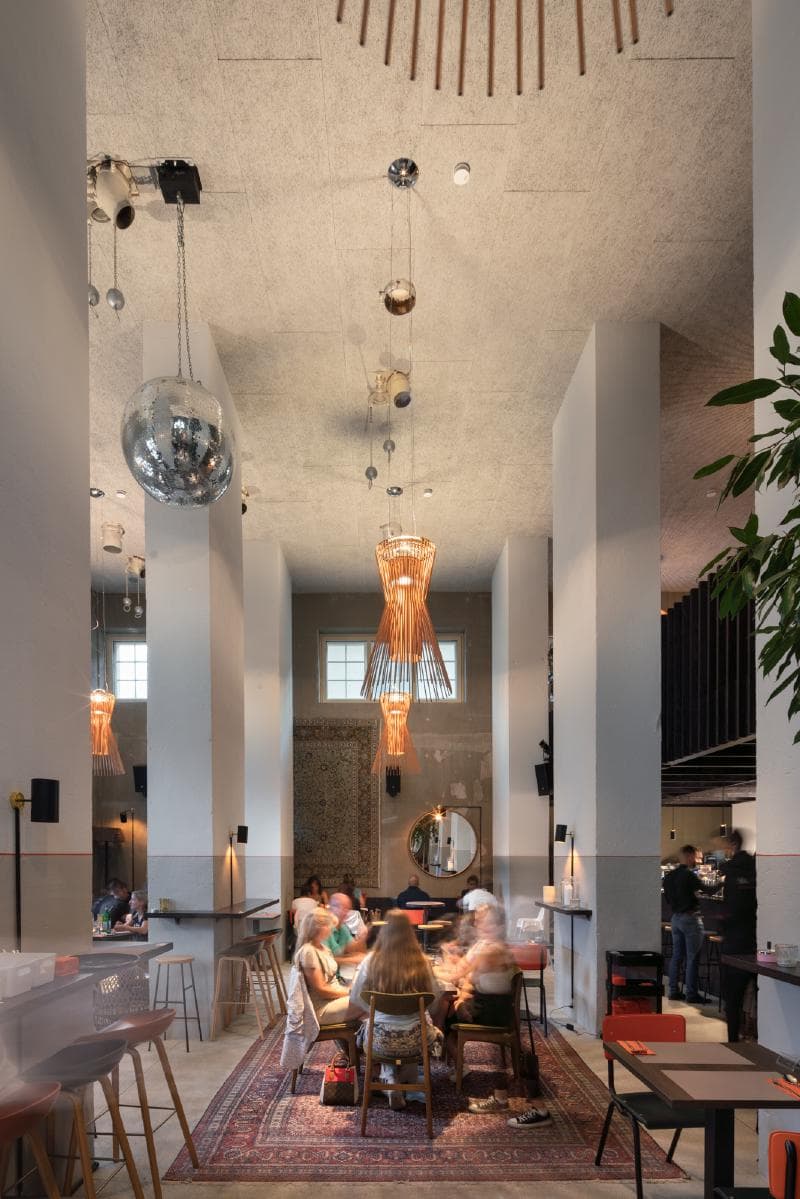 Architectural project - vibrant atmosphere, eclectic vibe, mix materials, mixed seating, modern dining, plant decor, stylish interior, vibrant setting, ceiling lights, pendant lighting, community dining, large mirror, eclectic decor, restaurant interior, cozy restaurant, group seating, industrial fixtures, urban dining, polished floors, trendy design, welcoming environment, decorative lighting, conversation nook, varied textures, chic setting, atmospheric light, mirror accent, relaxed dining, hanging lighting, decorative rug, diverse seating, conversational dining, inviting restaurant, communal table, bar area, modern lighting, wood elements, contemporary style, neutral colors, social space, beige tones, warm ambiance, airy space, open layout, inviting space, dining experience, casual dining, cozy corner, textured walls, high ceiling