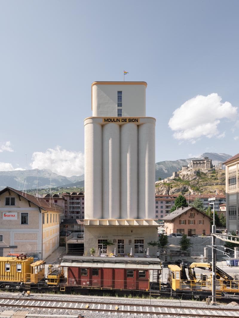 Architectural project - light grey, urban renewal, modern renovation, train station, urban revitalization, city center, urban integration, concrete facade, city skyline, heritage conservation, contextual design, mixed-use building, grain silo, converted building, renovated architecture, railway context, railway station, mountain backdrop, historical site, industrial heritage, vertical structure, urban landmark, blend of old and new, public transportation hub, modern adaptation, preservation architecture, sustainable urbanism, eco refurb, grey tones, urban setting, steel, cityscape, outdoor space, natural light, glass, grey, urban environment, industrial vibe, beige, brown, concrete, minimalist facade, neutral palette, minimalist design, adaptive reuse, panoramic view, exterior view, industrial building, architectural contrast