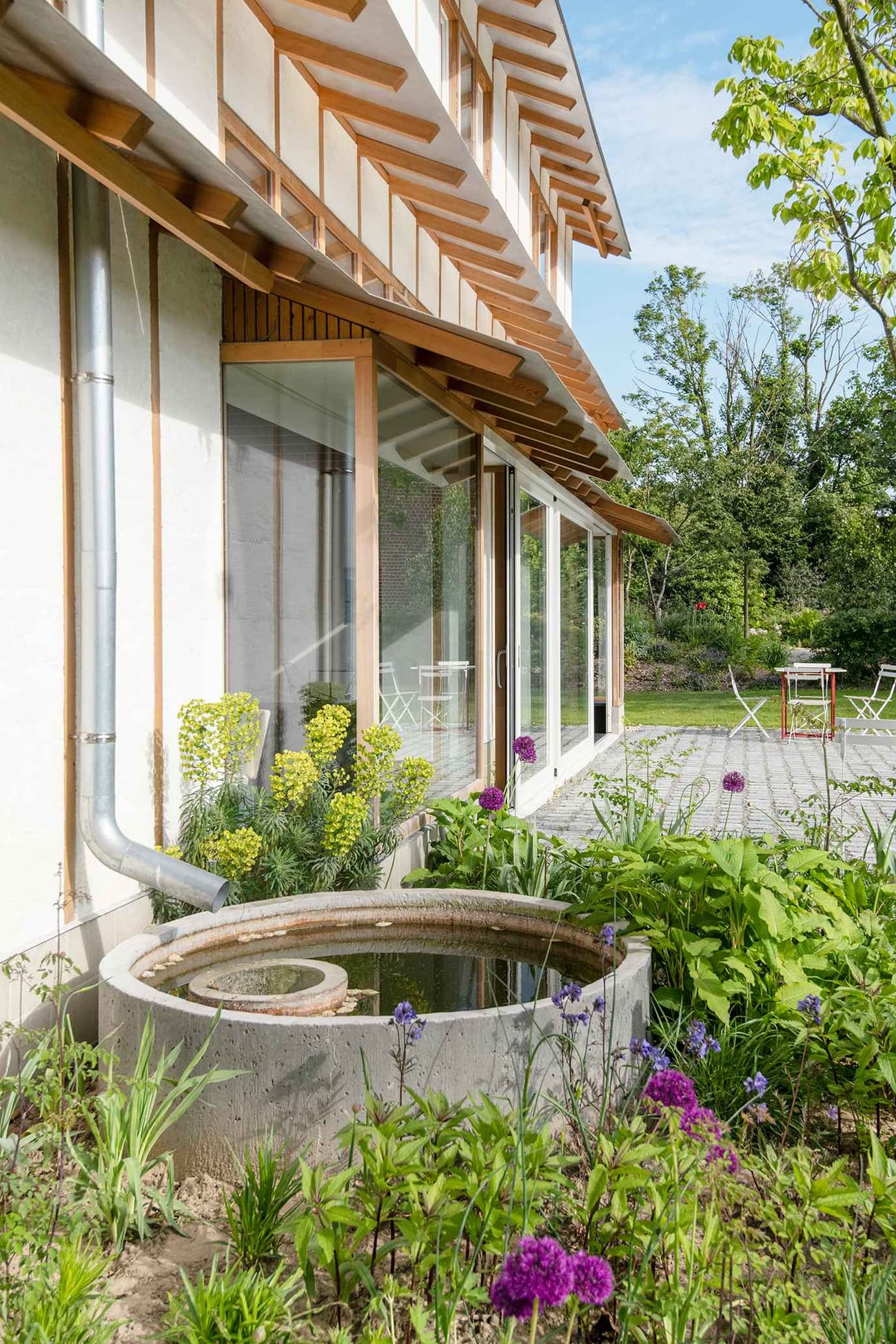 Architectural project - serene vibe, sustainable materials, wood, timber, steel, natural light, glass, green, neutral tones, daylight, brown, low carbon design, eco friendly, compact space, relaxed atmosphere, outdoor seating, glass doors, tranquil setting, natural landscape, green architecture, circular design, biophilic design, sustainable home, modern facade, white facade, large windows, indoor outdoor, timber cladding, white, plaster wall, energy efficient, plaster, green home, garden design, nature integration, eco house, wooden structure, wooden slats, seamless transition, lush greenery, biodiversity, garden pond, water feature, passive solar, residential garden, outdoor retreat, home garden, comfortable living, cozy outdoors, modern nature