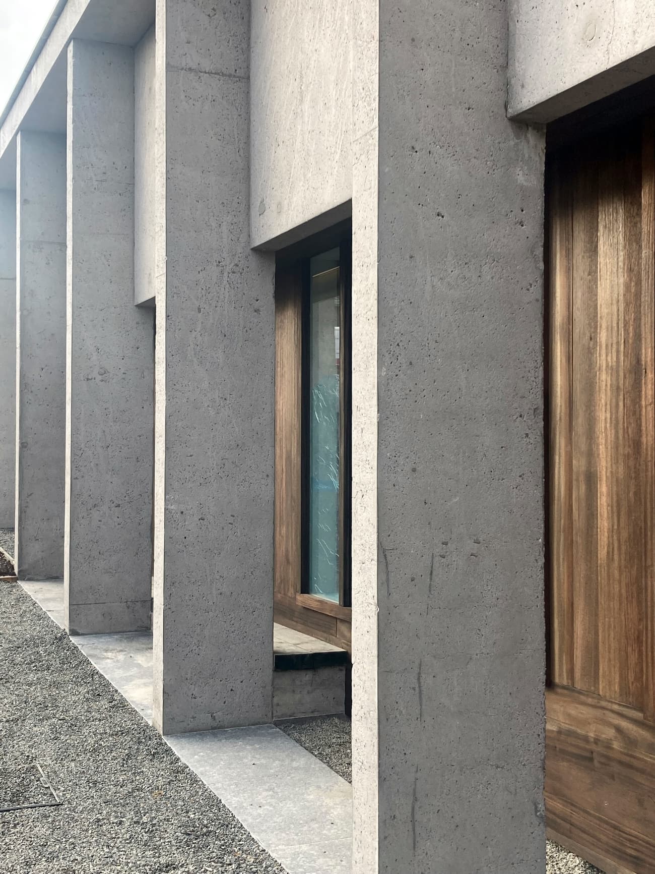 Architectural project - exposed concrete, geometric lines, raw concrete, vertical lines, grey facade, wooden doors, concrete facade, minimal vibe, grey concrete, brutalist architecture, brutalist, sustainable materials, wood, timber, outdoor space, sustainable design, modular design, grey, brown, concrete, architectural elements, exterior wall, industrial style, low carbon design, functional design, daylight optimization, natural textures, contemporary design, minimalist design, open facade, urban design, passive house, natural ventilation, modern facade, clean lines, architectural simplicity, energy efficient, wood accents, timber accents, earthy tones, eco-friendly building, sleek design, facade design, concrete wall, structural rhythm, contemporary building
