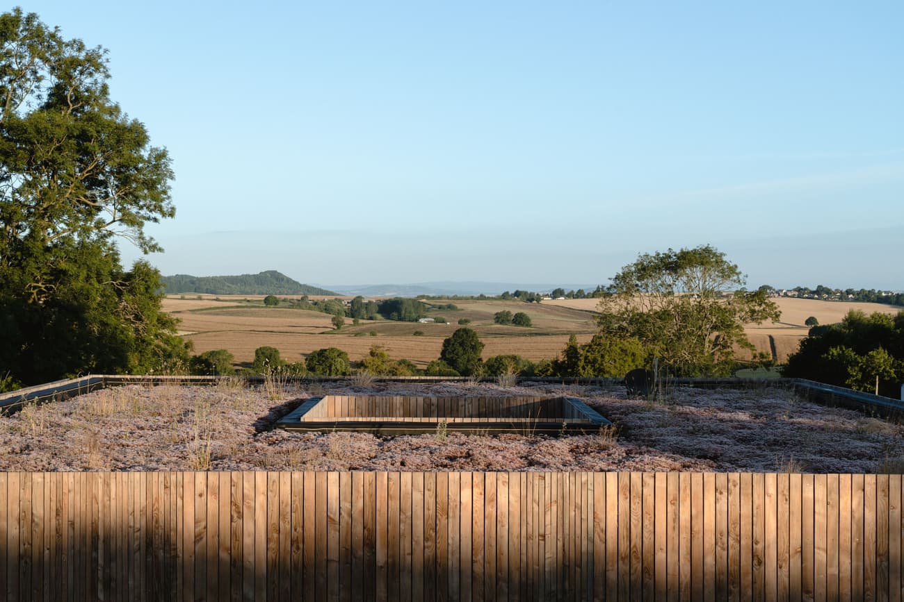 Architectural project - sustainability, rural landscape, open sky, countryside charm, horizon view, roof garden, eco roof, wooden fence, timber fence, wood barrier, distant hills, meadow views, pastoral beauty, morning light, scenic beauty, native vegetation, ecosystem integration, natural materials, eco-friendly design, wood, timber, outdoor space, warm sunlight, passive design, sustainable design, green, neutral tones, landscape architecture, brown, natural setting, serene atmosphere, circular design, earth tones, scenic view, countryside view, panoramic view, environmental design, tranquil vibe, rural setting, landscape design, nature integration, green roof, organic textures, outdoor relaxation