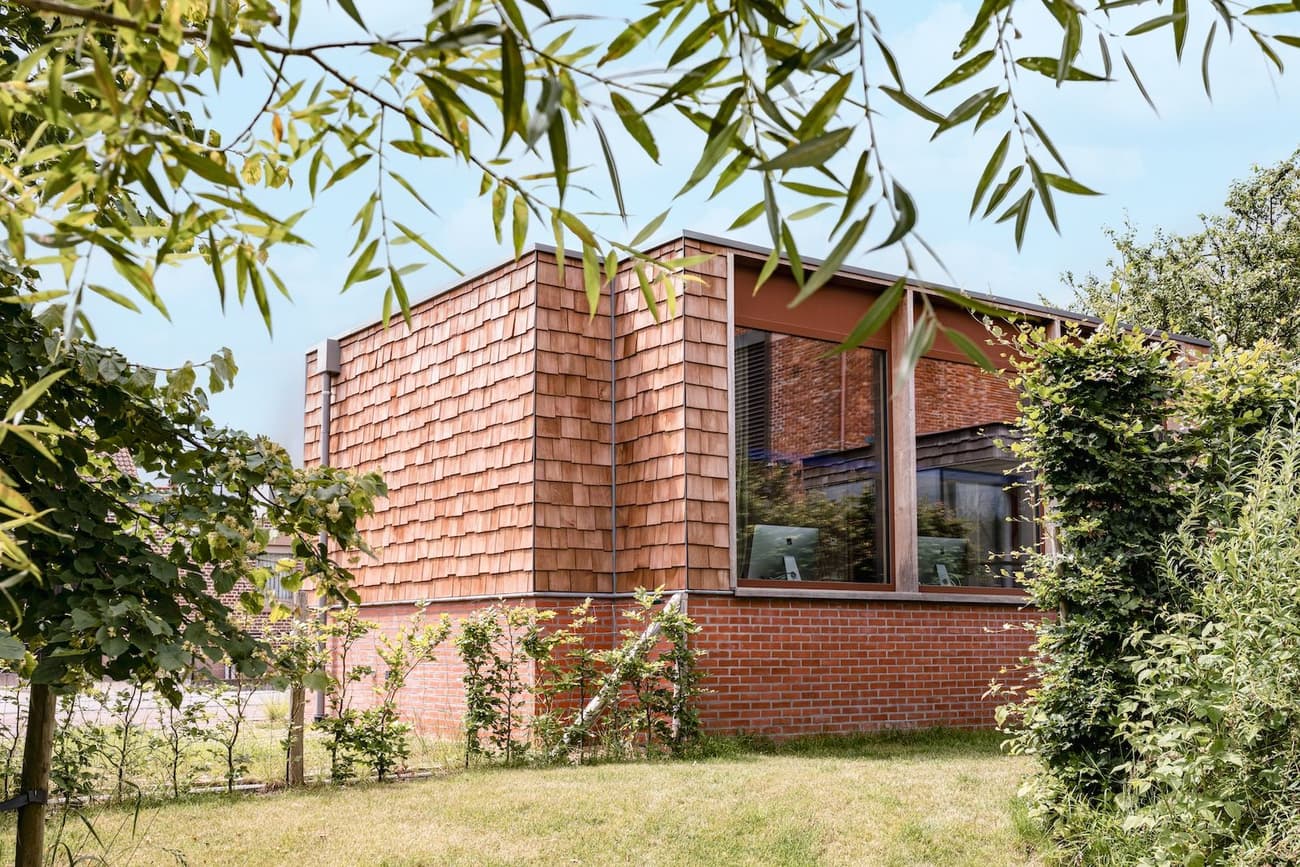 Architectural project - brick wall, brick house, landscaping, seamless blend, single story, natural materials, sustainable materials, wood, timber, raw materials, outdoor space, natural light, passive design, sustainable design, warm tones, natural tones, green, daylight, brown, architectural elements, flat roof, minimalist design, earthy texture, biophilic design, contemporary home, timber cladding, eco friendly home, green home, exterior elements, terracotta, brick, brick facade, exterior view, garden view, residential architecture, nature integration, cozy exterior, eco house, modern home, warm exterior, shingle facade, timber wall, modern exterior, suburban home, simple form, rectangular form, outdoor greenery, red